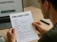 A student checks a printed ATMA admit card beside a laptop before exam day.